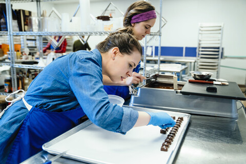 Weibliche Mitarbeiter bereiten Pralinen am Tisch in einer Fabrik vor, lizenzfreies Stockfoto
