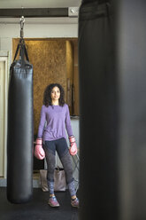 Porträt einer weiblichen Boxerin am Boxsack im Fitnessstudio - CAVF58833