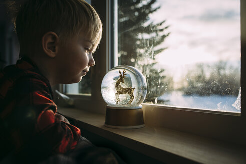 Seitenansicht eines Jungen, der die Dekoration auf der Fensterbank zu Hause betrachtet - CAVF58852