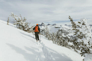 Rückansicht eines Wanderers mit Rucksack und Skistöcken beim Wandern auf einem schneebedeckten Berg - CAVF58876