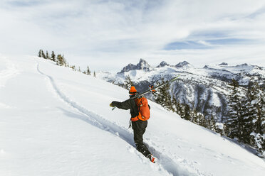 Wanderer trägt Ski auf der Schulter, während er einen schneebedeckten Berg besteigt - CAVF58882