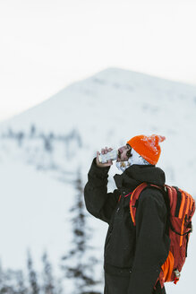 Seitenansicht eines Wanderers mit Rucksack, der aus einer Dose trinkt, während er vor einem schneebedeckten Berg steht - CAVF58883
