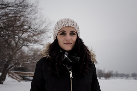 Lächelnde Frau, die wegschaut, während sie im Winter gegen den Himmel steht, lizenzfreies Stockfoto