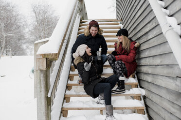 Happy friends talking while sitting on snow covered steps - CAVF58898