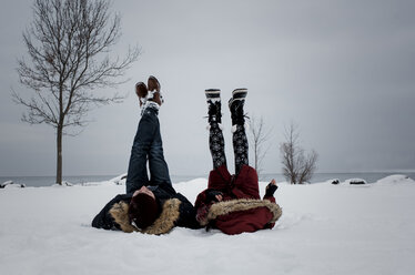 Freunde liegen am schneebedeckten Strand gegen den Himmel im Winter - CAVF58902