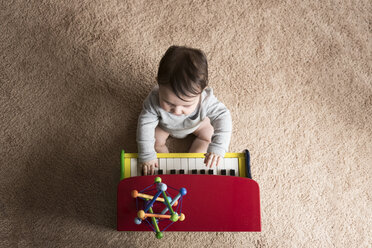 Overhead view of baby boy playing toy piano on carpet at home - CAVF58919