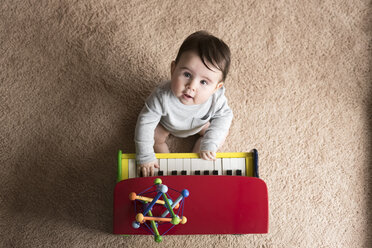 Overhead portrait of cute baby boy playing toy piano on carpet at home - CAVF58920