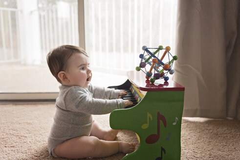 Seitenansicht eines neugierigen kleinen Jungen, der zu Hause Spielzeugklavier spielt - CAVF58921