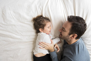 Blick von oben auf einen fröhlichen Vater und eine Tochter, die zu Hause auf dem Bett liegen - CAVF58924