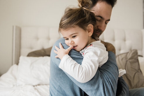Liebender Vater umarmt Tochter auf dem Bett zu Hause - CAVF58925