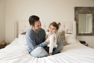 Porträt einer fröhlichen Tochter mit ihrem Vater, der zu Hause auf dem Bett sitzt - CAVF58926