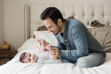 Vater spielt mit seinem Sohn, während er zu Hause auf dem Bett sitzt - CAVF58929