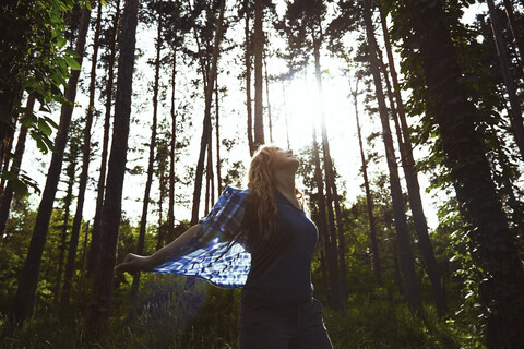 Unbekümmerte Frau, die ein Hemd hält, während sie inmitten von Bäumen im Wald steht, lizenzfreies Stockfoto