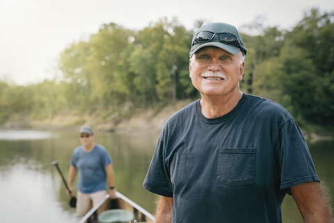 Porträt eines älteren Mannes, der mit einem Freund ein Boot in Richtung Seeufer schiebt, lizenzfreies Stockfoto