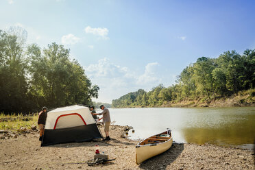 Male friends standing by tent at lakeshore against sky - CAVF59001