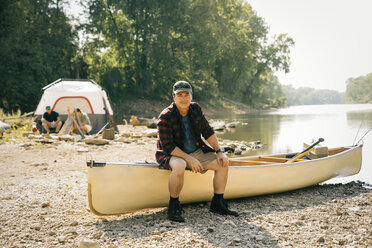 Porträt eines mittleren erwachsenen Mannes, der auf einem Boot sitzt, mit Freunden im Hintergrund auf einem Campingplatz - CAVF59004