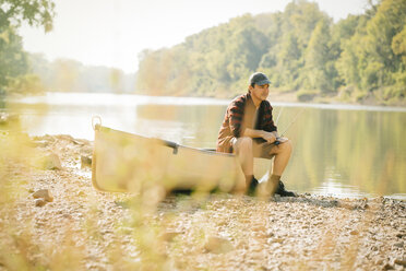 Mittlerer erwachsener Mann schaut weg, während er auf einem Boot am Seeufer sitzt - CAVF59005