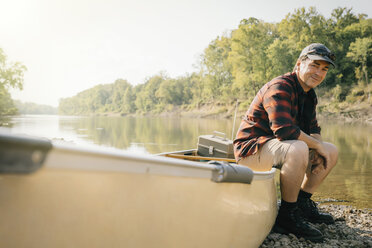 Porträt eines lächelnden erwachsenen Mannes, der auf einem Boot am Seeufer sitzt - CAVF59007