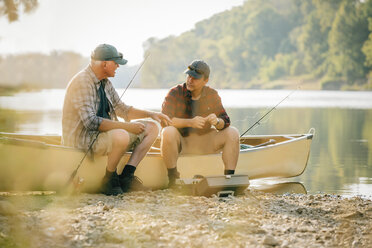 Freunde unterhalten sich, während sie mit Angelruten auf einem Boot am Seeufer sitzen - CAVF59021
