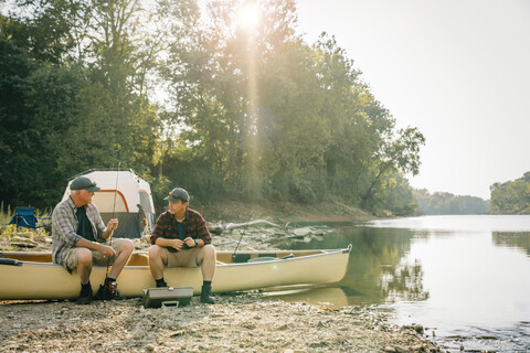 Freunde mit Angelruten unterhalten sich auf einem Boot auf dem Campingplatz, lizenzfreies Stockfoto