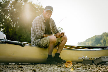 Portrait of smiling senior man with fishing rod sitting on boat against clear sky - CAVF59027