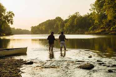 Rear view of male friends walking in lake against clear sky during sunset - CAVF59039