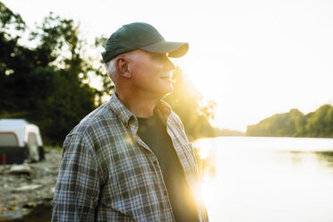 Älterer Mann, der bei Sonnenuntergang am Seeufer vor einem klaren Himmel steht und wegschaut - CAVF59046
