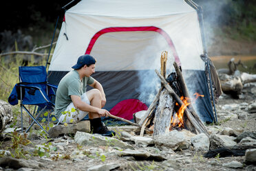 Seitenansicht eines jungen Mannes, der während des Sonnenuntergangs auf dem Campingplatz sitzt - CAVF59050