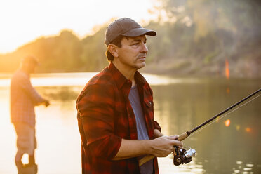 Mid adult man looking away while friend fishing in background during sunset - CAVF59058