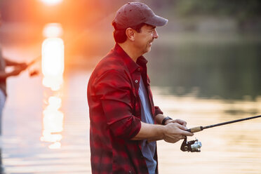 Side view of teenage boy fishing with rod in lake while standing against  cloudy sky stock photo