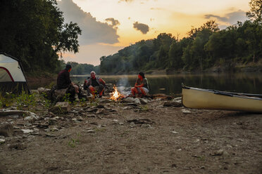 Friends talking while camping by lake against sky during sunset - CAVF59069