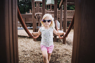 Porträt eines Mädchens mit Sonnenbrille, das auf einem Spielplatz steht - CAVF59073