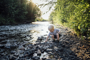 Junge spielt mit Kieselsteinen und hockt am Fluss - CAVF59111