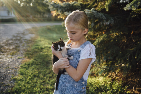 Mädchen hält Katze auf einem Feld stehend - CAVF59114