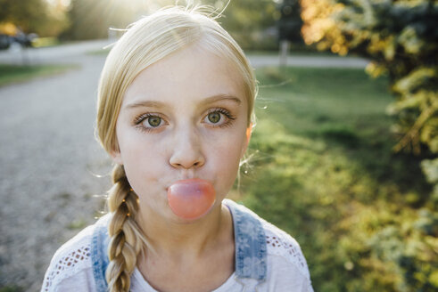 Porträt eines Mädchens, das auf einem Feld stehend Kaugummi bläst - CAVF59116