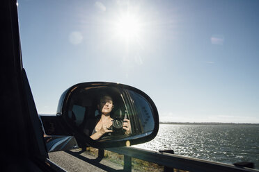 Frau beim Fotografieren, während sie sich im Seitenspiegel eines Autos gegen den Himmel spiegelt - CAVF59143