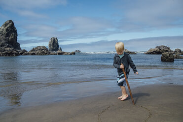 Junge macht Kreis auf Sand mit Stock am Strand - CAVF59147