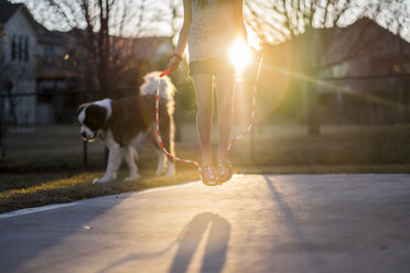 Low section of girl jumping rope at playground with dog in background - CAVF59166