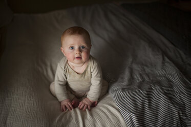 High angle portrait of cute baby boy sitting on bed in darkroom - CAVF59168