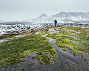 Blick aus der mittleren Entfernung auf einen Wanderer, der auf einer Wiese vor schneebedeckten Bergen im Winter steht - CAVF59178