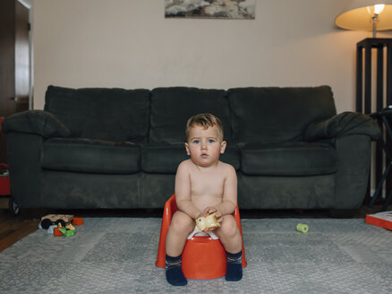 Porträt eines niedlichen, hemdsärmeligen kleinen Jungen, der auf dem Töpfchen sitzt und gegen das Sofa im Wohnzimmer uriniert - CAVF59189