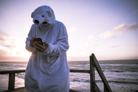 Dänemark, Nordjuetland, Mann im Eisbärenkostüm am Strand, mit Smartphone, lizenzfreies Stockfoto