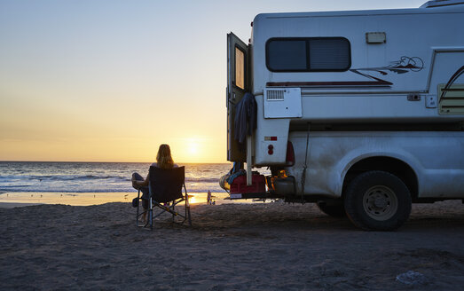 Chile, Arica, Frau sitzt neben Wohnmobil am Strand bei Sonnenuntergang - SSCF00079