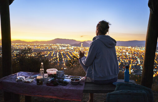 Chile, Santiago, woman drinking a beer in the mountains above the city at sunset - SSCF00090