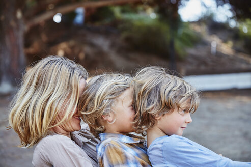 Glückliche Mutter mit zwei Söhnen, die in einer Reihe im Freien sitzen - SSCF00100