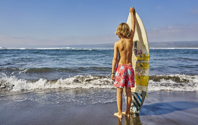 Chile, Pichilemu, Junge am Meer stehend mit Surfbrett - SSCF00120