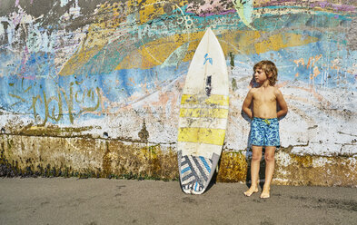 Chile, Pichilemu, boy standing at a colorful wall with surfboard - SSCF00123