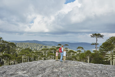 Chile, Puren, Nahuelbuta-Nationalpark, Frau steht mit Söhnen auf einem Felsblock und schaut auf Araukarienwald - SSCF00151