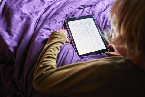 Boy reading e-book on tablet in bed stock photo