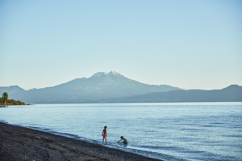 Chile, Lago Llanquihue, Vulkan Calbuco, zwei Jungen spielen im Wasser, lizenzfreies Stockfoto